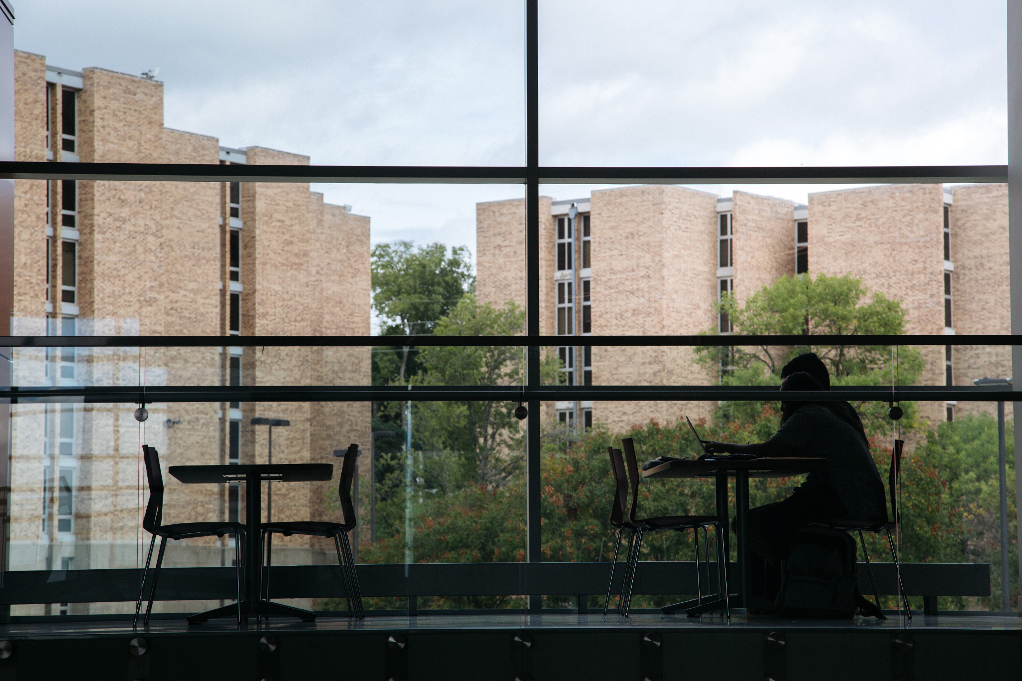 Person sitting at a table, next to a window with a view of campus buildings outside